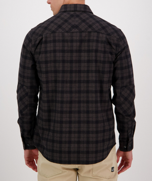 Wearing a Swanndri Port Road Shirt in dark plaid with long sleeves and beige pants, a person stands with their back to the camera against a plain, light background.