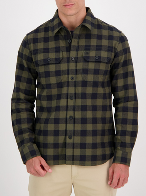 A man wearing the Swanndri Taranaki Tailor Shirt, a green and black checkered long-sleeve 100% cotton flannel, with beige pants, stands against a plain white background.