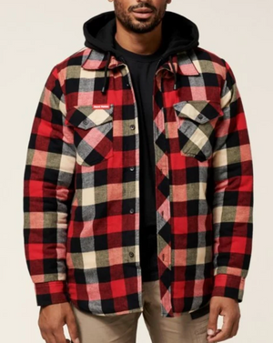 A man is wearing the Hard Yakka Quilted Flannelette Shacket, featuring a durable plaid pattern with two chest pockets and button closures, layered over a black hoodie. He has paired this ensemble with light brown pants. The scene is set against a plain, light-colored background.