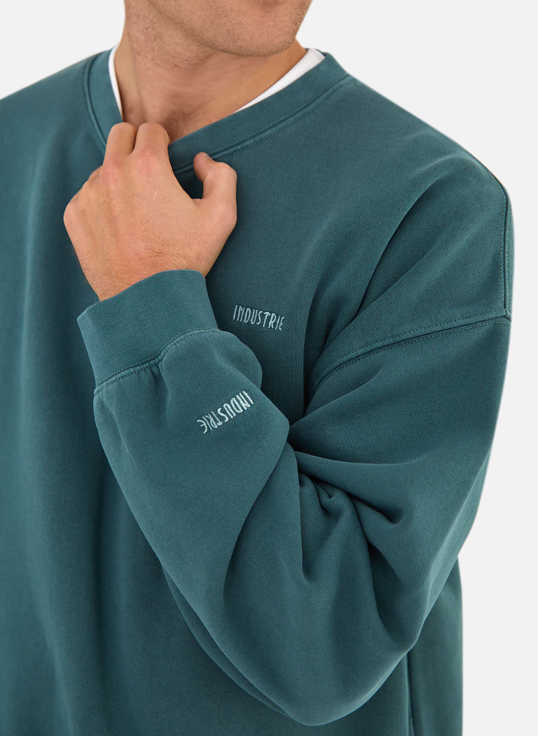 Wearing the "Industrie The Del Sur Sweat," featuring the logo on chest and sleeve, a person casually tugs at the neckline, adding a relaxed vibe to the oversized comfort jumper against a plain background.