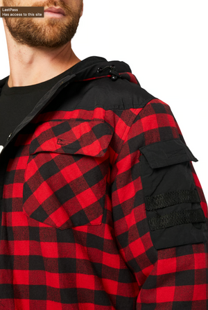 A person with a beard sports the CAT Sequoia Shirt Jacket, a red and black checkered cotton piece featuring buttoned chest pockets, fleece lining for warmth, and stylish black fabric arm patches. They wear a black hood and shirt underneath.