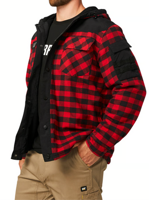 Someone wearing the CAT Sequoia Shirt Jacket, a red and black plaid jacket with cozy fleece lining and black accents, stands with a hand in the pocket of beige cargo pants. The top of a logo on a black shirt is visible under the jacket.
