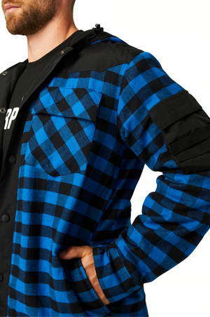 A person wearing the CAT Sequoia Shirt Jacket—blue and black checkered with durable overlays on shoulders and sleeves—stands with one hand in their pocket, upper body visible.