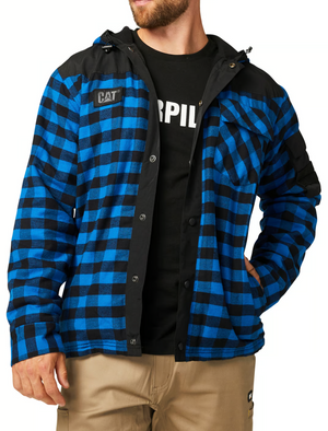 A man wears the CAT Sequoia Shirt Jacket, a blue and black plaid jacket with durable overlays, black shoulder accents, a fleece-lined hood, and "CAT" logo, partially unbuttoned over a black Caterpillar T-shirt and tan pants.
