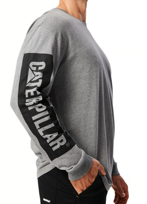 A person is wearing the CAT Icon Block Long Sleeve Tee, which is gray and made of 100% cotton. It features "CAT" in bold black letters down the sleeve. The image shows them from the neck down, also displaying black pants.