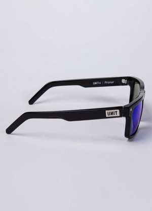 Side view of UNIT Primer Polarised Eyewear showcasing a rectangular, lightweight black frame. The straight arms feature the "UNIT" brand name, and the polarized lenses have a reflective blue tint with UV protection. The background is light gray.