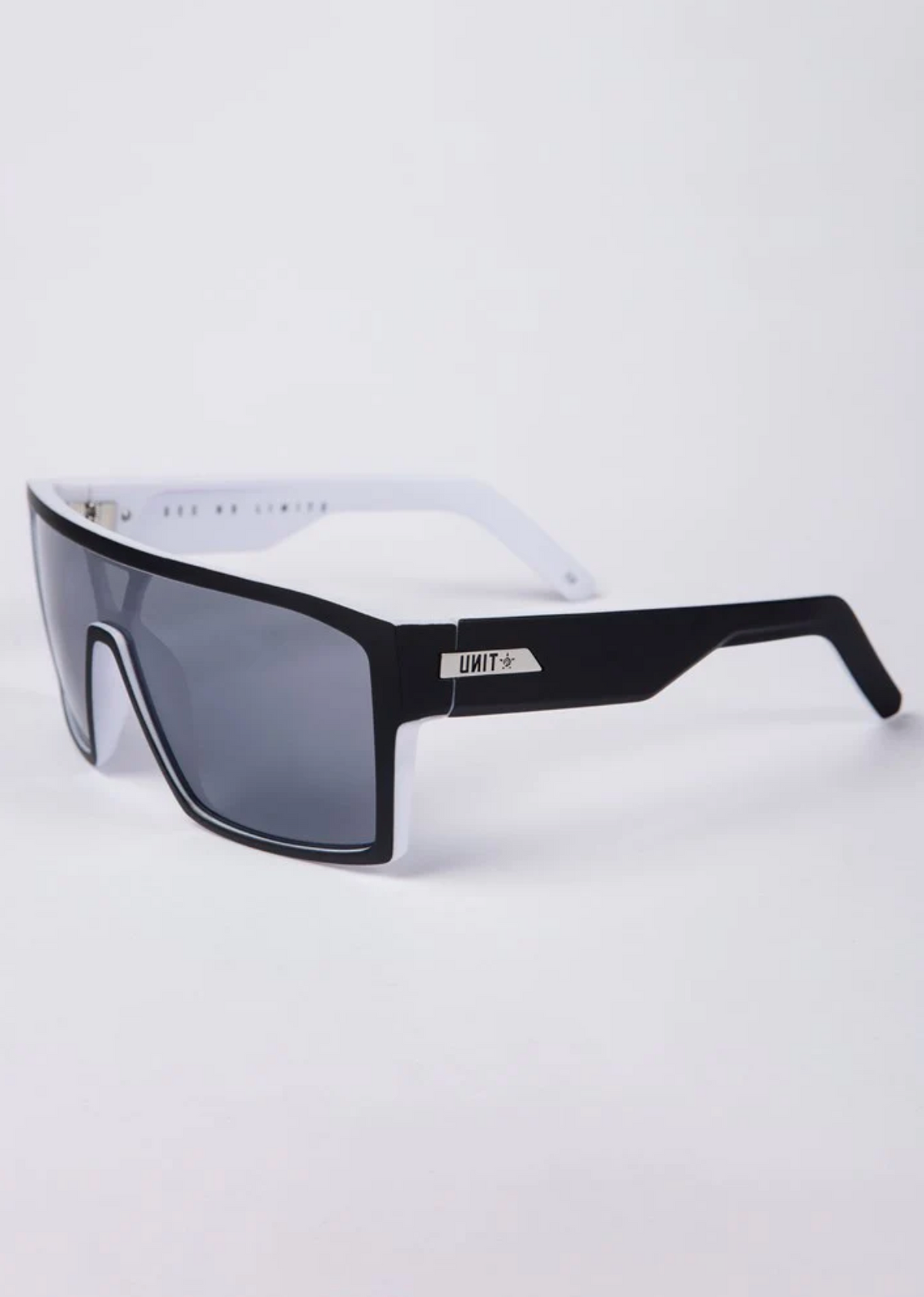 UNIT Command Polarised Eyewear features rectangular black frames, gray lenses, and white lightweight arms. The left arm displays a metallic "UNIT" tag with a star logo. Provides UV protection. Set against a plain white background.