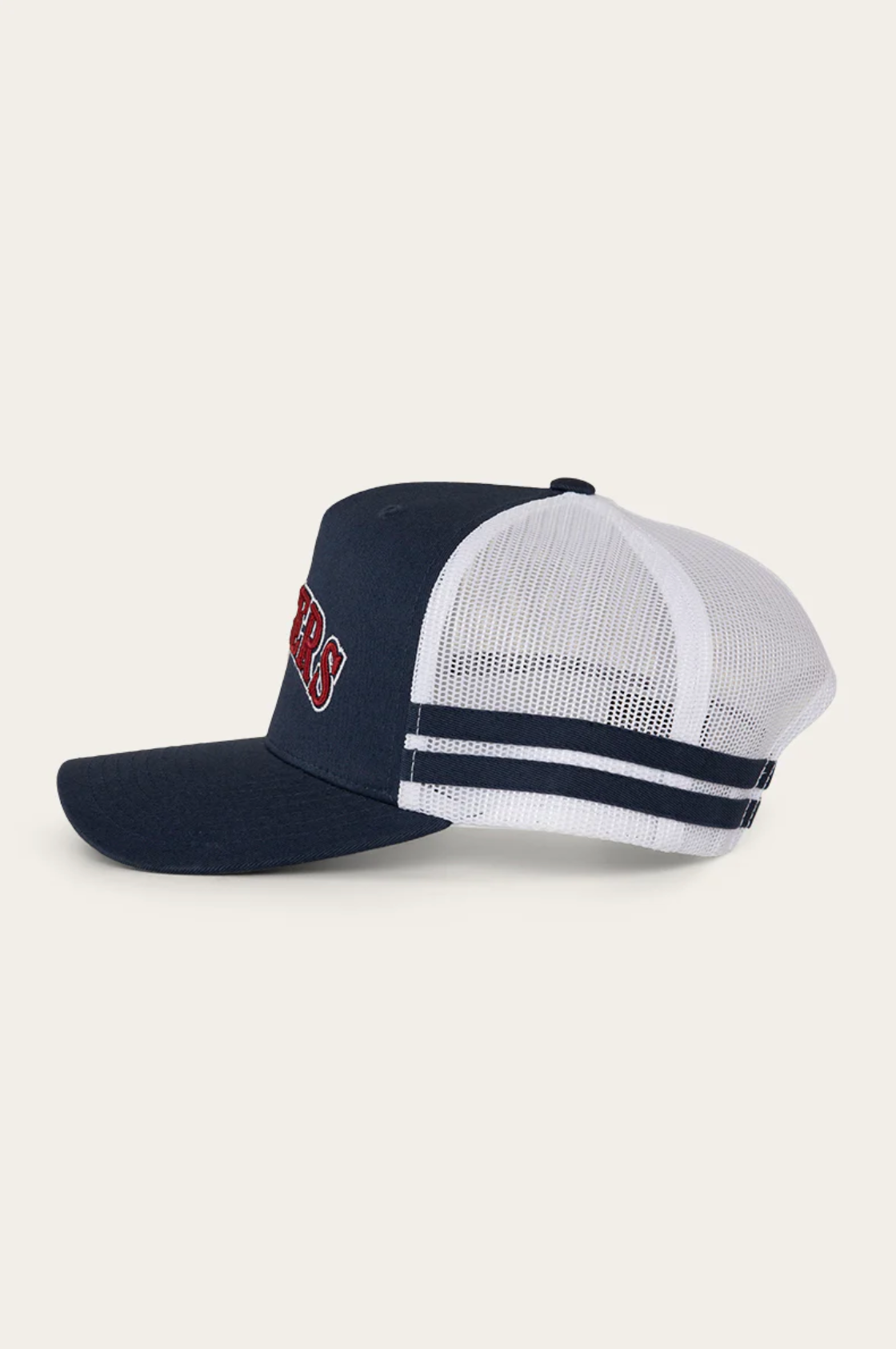 The Ringers Western Caleb Trucker Cap features a navy blue and white design with a mesh back, cotton twill navy bill, two navy stripes on the white adjustable strap, and red and white embroidered lettering on the front.