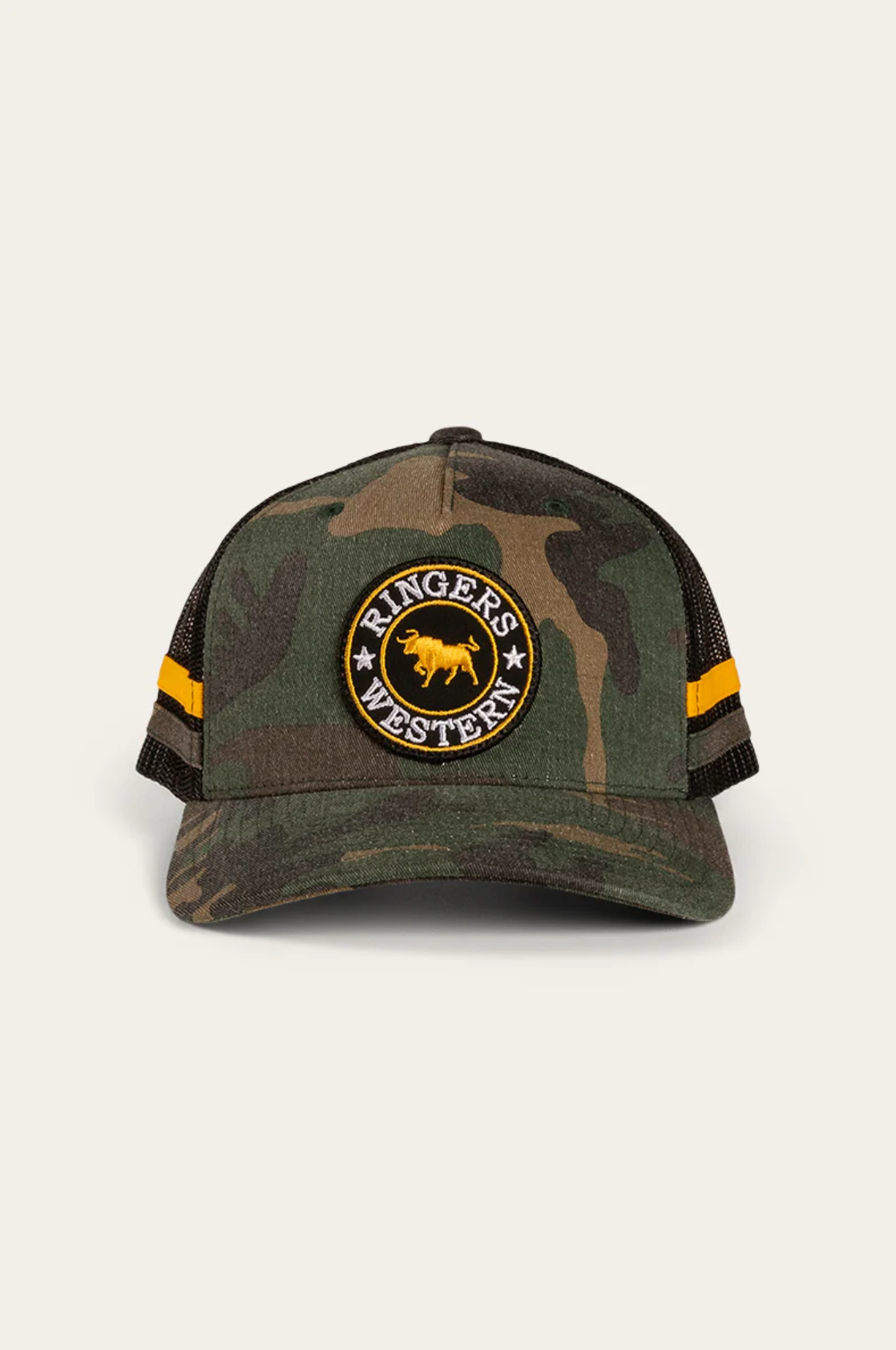The Ringers Western McCoy Kids Trucker Cap features a camouflage pattern with a black mesh back and adjustable strap. It has a front circular patch with a yellow bull and "Ringers Western" text, plus two yellow stripes on each side of the mesh.