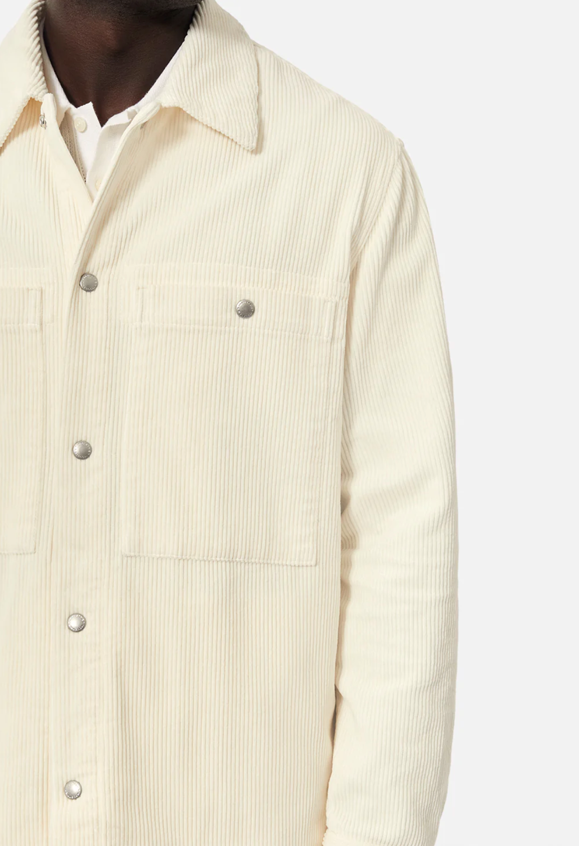 Wearing Industrie The Atmore Jacket, a cream corduroy jacket with stylish detailing and silver buttons, this person pairs it with a white shirt. Made of 100% cotton, it features two chest pockets and is photographed against a plain background.