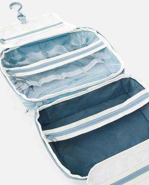 The Rip Curl Paradise F-Light Beauty Case in light blue is open, displaying several zippered compartments and clear pockets for organizing personal items. Crafted from recycled polyester, it’s a stylish and eco-friendly choice for travel.