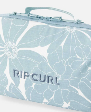 The Rip Curl Paradise F-Light Beauty Case is a light blue and white bag with a floral pattern, "RIPCURL" embroidered on the front, a top handle and zipper, and is made from recycled polyester.