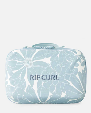 The Rip Curl Paradise F-Light Beauty Case is light blue with white floral patterns, made from recycled polyester, featuring an embroidered "RIP CURL" logo, and includes a matching top zipper and handle.