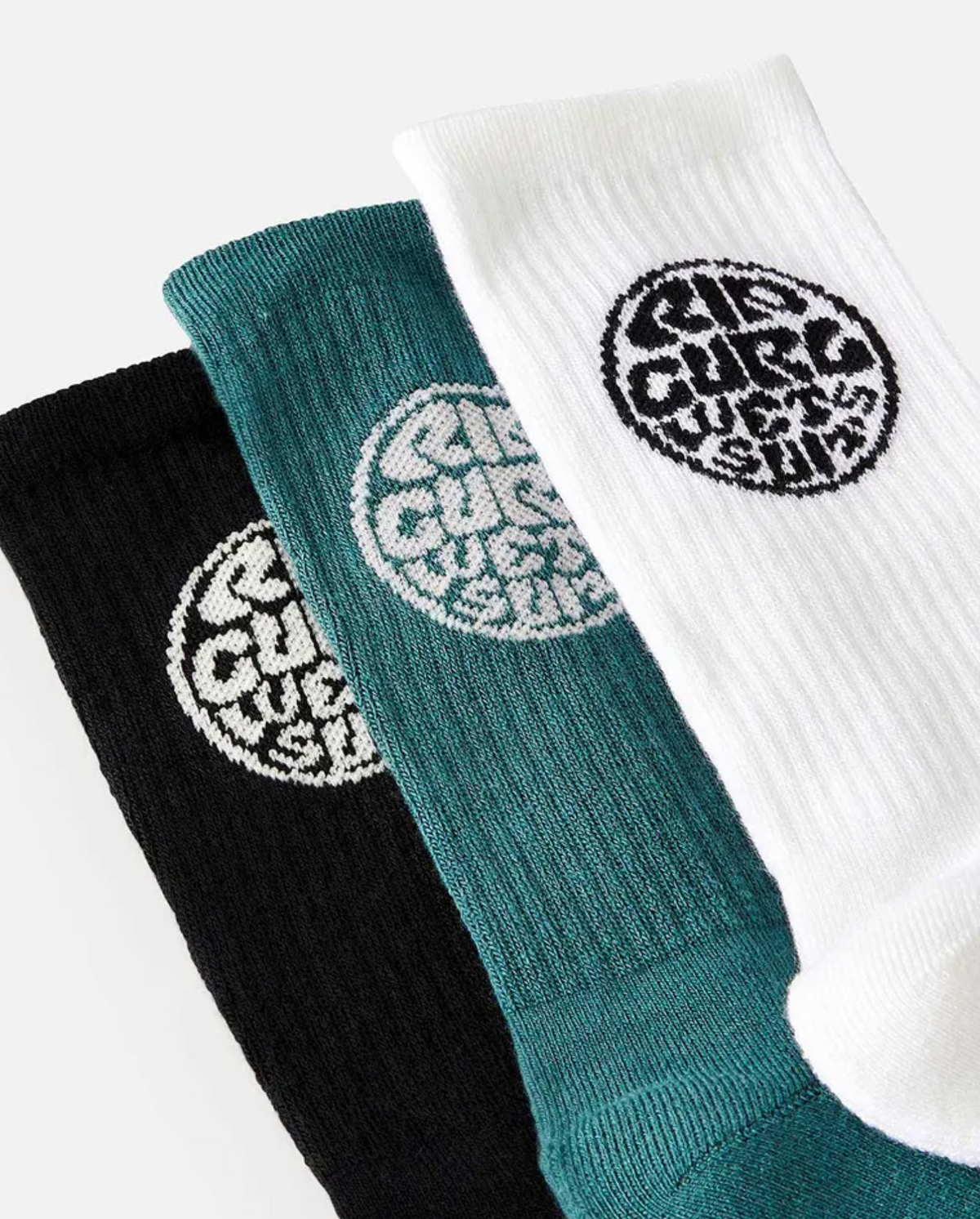 The Rip Curl Wetty Crew Sock 3 Pack, featuring black, teal, and white socks with circular logo patterns, is showcased against a plain background. These socks are crafted from an acrylic blend and arranged in a fanned display.