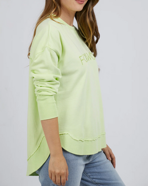 A woman in the Foxwood Simplified Crew, a relaxed fit light green cotton sweatshirt with raw hem details, paired with light blue jeans, stands sideways against a plain background.