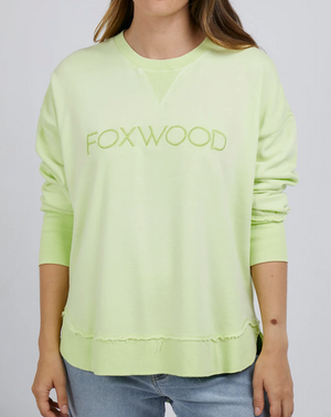 Wearing the Foxwood Simplified Crew, a light green cotton sweatshirt with Foxwood embroidery, paired with light blue jeans. The relaxed fit is shown in a photo cropped at the neck and thighs.
