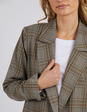 A person in the Foxwood Beatrix Blazer with button details over a white top holds the lapel; their face is partly visible, showing light wavy hair and natural makeup.