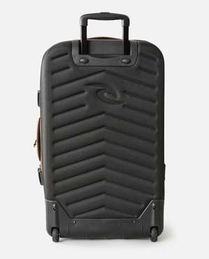 The Rip Curl F-Light Global 110L Searchers Travel Bag is a black hard-shell bag with a chevron pattern, extendable handle, durable inline skate wheels, and an embossed Rip Curl logo on the front.