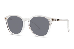Liive Berawa Sunglasses feature clear round frames, dark gray UV-protective lenses, and a minimal modern design. Crafted from lightweight polycarbonate, they are presented on a plain white background.