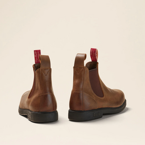 The Rossi Booma 607 Elastic Sided Boot features a pair of brown Chelsea boots made from Full Grain Australian Leather and equipped with black, slip-resistant soles. They are designed with red pull tabs on the back and elastic side panels for easy wear. Positioned on a light beige background, the boots are displayed showcasing both the side and back views.