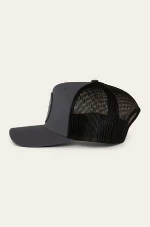 The Ringers Western Signature Bull Trucker Cap, in black and dark gray cotton twill with a curved brim and mesh back, is shown from the side against an off-white background.