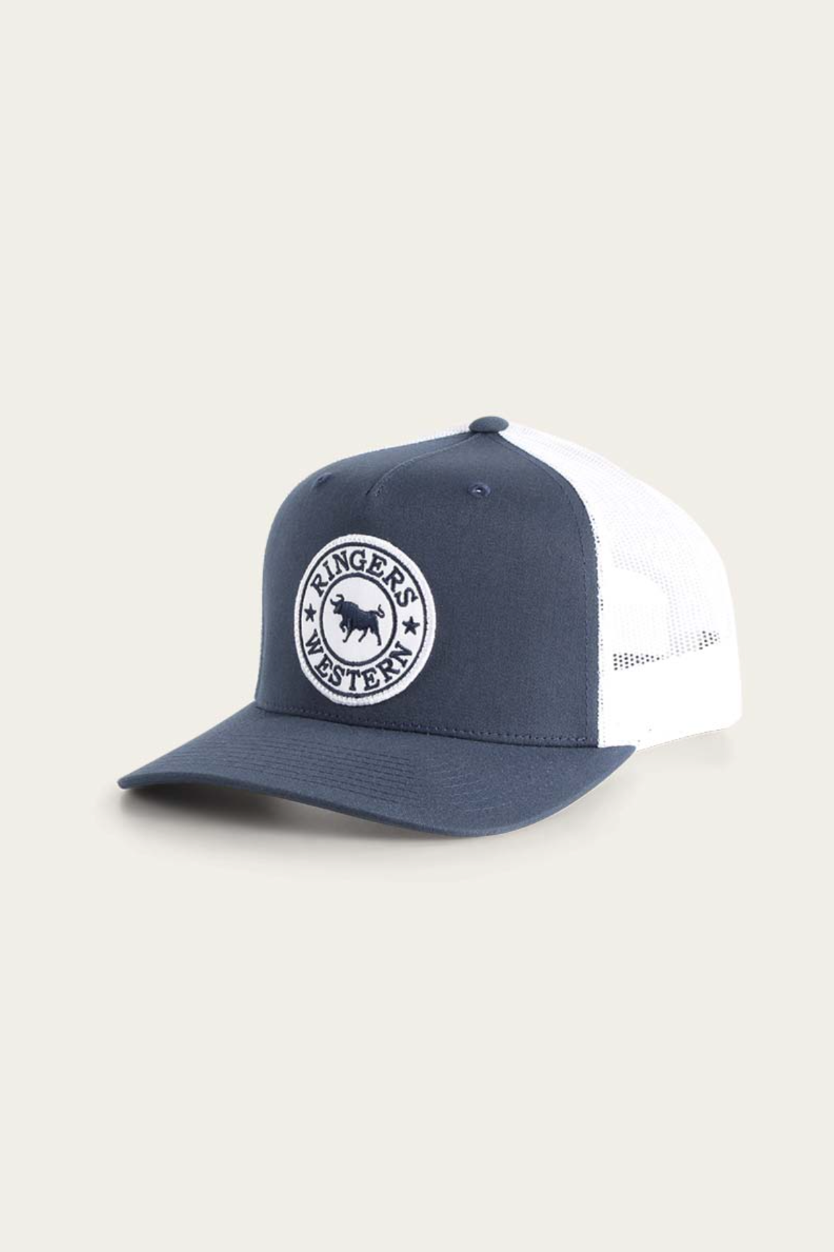 The Ringers Western Signature Bull Trucker Cap is a blue and white trucker cap made of durable cotton twill, featuring a breathable mesh back and a light beige circular patch with stars and "Ringers Western" on the front.