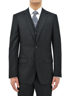A person is standing with arms by their sides, dressed in a dark grey Boston Michel Jacket paired with a matching vest. They are also wearing a white dress shirt and a patterned tie. The comfort fit suit jacket features two buttons and the background is plain white.