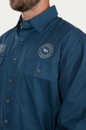 A person is wearing a blue Ringers Western Hawkeye Embroidered Shirt with UPF50+ protection, featuring the brand's logo on the chest pocket, complete with a collar and long sleeves against a white background.