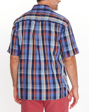 A person wearing a Breakaway Rome Bamboo Blend Shirt, a short-sleeved blue and red plaid casual shirt made from comfortable bamboo polyester, stands with their back to the camera. They're also in red pants against a plain white background.