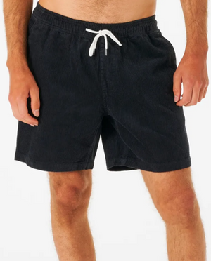 Wearing Rip Curl Surf Revival Cord Volley shorts with a white drawstring, a person stands against a plain backdrop. Only their lower torso and legs in the baggy fit black corduroy shorts are visible, evoking 90's style charm.