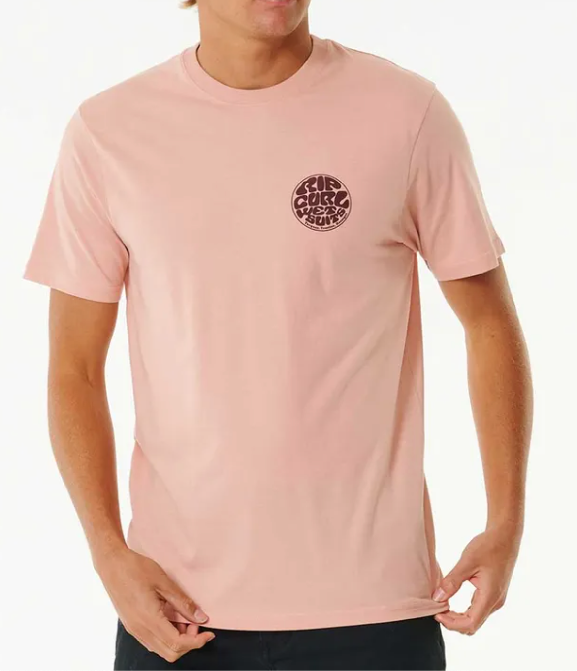 Wearing a light pink Rip Curl Wetsuit Icon Tee, featuring a small circular graphic logo on the left chest. Made from 100% cotton, this comfortable casual tee is held at the bottom by both hands.