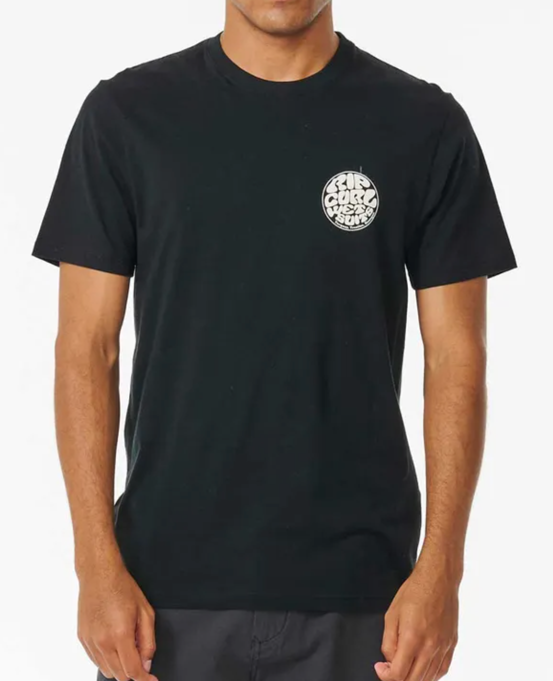 A man wears the Rip Curl Wetsuit Icon Tee, a comfortable 100% cotton shirt with a small circular white graphic and text on the left chest, standing against a white background.
