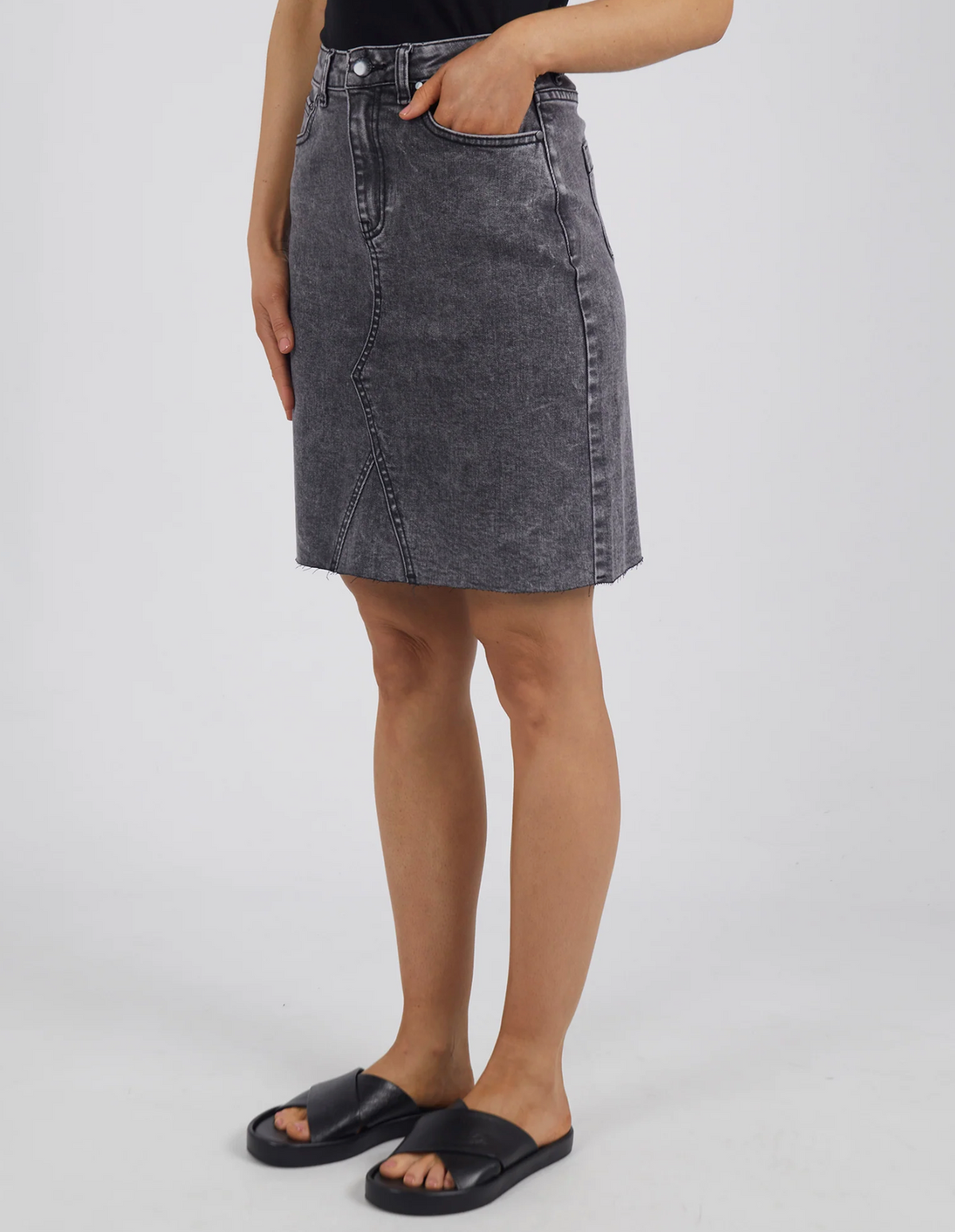 Donning a black top and the knee-length gray Foxwood Belle Skirt with a diagonal seam and A-line fit, complemented by a hand in the pocket and black slide sandals, they showcase effortless style.