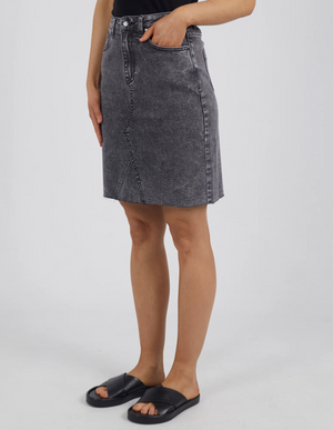 Donning a black top and the knee-length gray Foxwood Belle Skirt with a diagonal seam and A-line fit, complemented by a hand in the pocket and black slide sandals, they showcase effortless style.