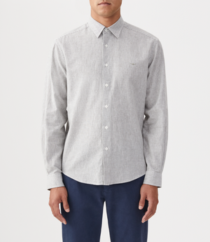 A person wears the RM Williams Coalcliff Shirt in light gray with long sleeves and dark blue pants, standing against a plain white background. The shirt has a small embroidered logo on the left chest.