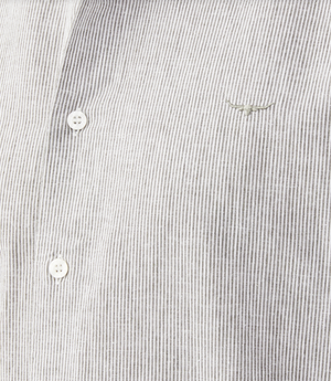 Close-up of an RM Williams Coalcliff Shirt in light grey with stripes, featuring three white buttons and thin vertical lines. A small longhorn embroidery resembling a bull's head adds a unique touch to the upper right of this classic shirt.