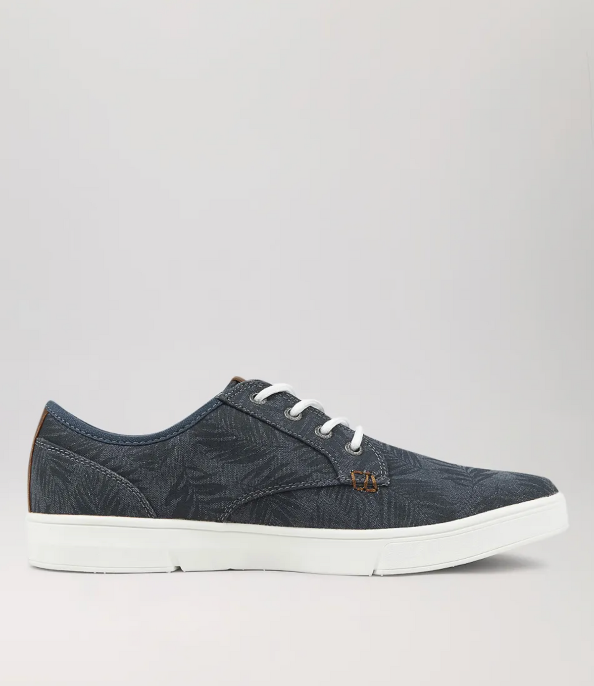 The Colorado Albatross Canvas Sneaker is a dark blue casual shoe with a wide fit, white sole, and subtle leaf patterns. It features white laces, brown details near the ankle and eyelets, a memory foam insole, and a textured grey background.