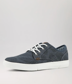 The Colorado Albatross Canvas Sneaker is navy blue with a subtle leaf pattern, white laces, and a white sole. It includes a memory foam inner sole for wide-fit comfort and is showcased against a plain gray background from a side angle.