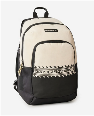 The Rip Curl Ozone 2.0 30L Backpack is crafted from recycled polyester in black and beige with a Greek key pattern at the bottom. It features multiple zippered compartments, a laptop section, and a top black handle, with the Rip Curl logo displayed on the upper beige area.