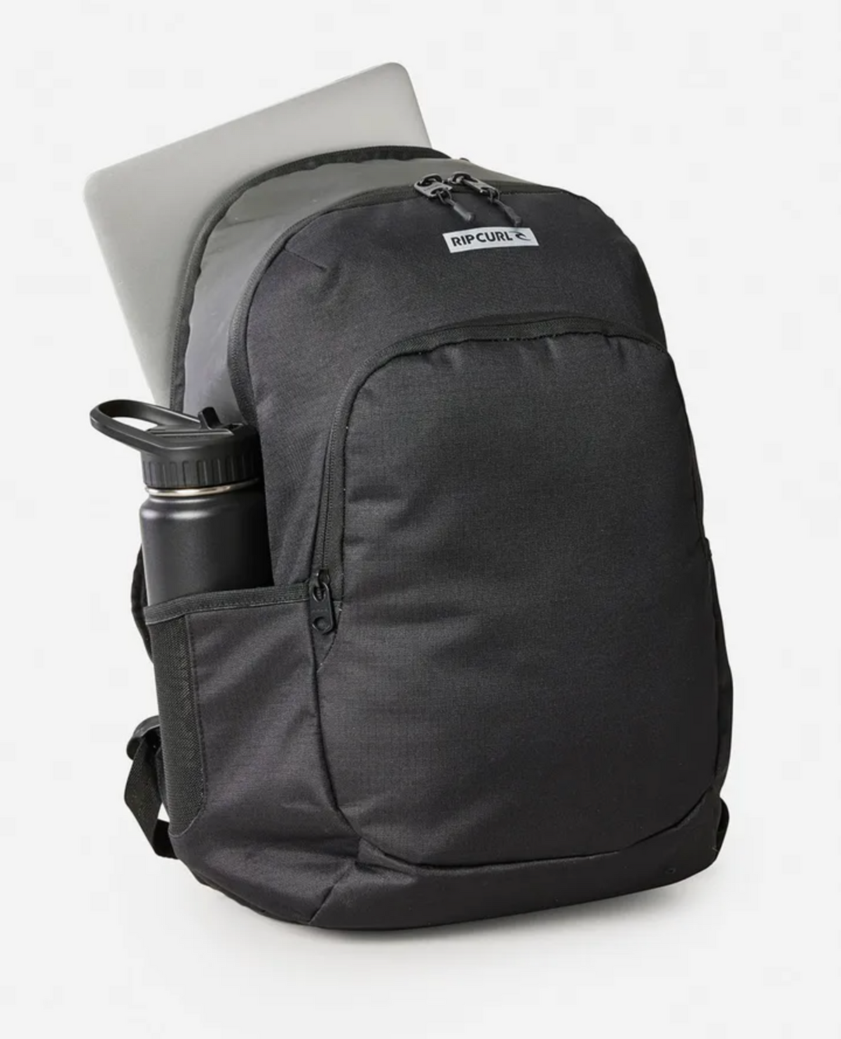 The Rip Curl Ozone Icons 30L Backpack in black holds a laptop in its back compartment and a water bottle in the side pocket. Made from recycled polyester, it features a top brand label. The sleek design stands out against the plain, light-colored background.