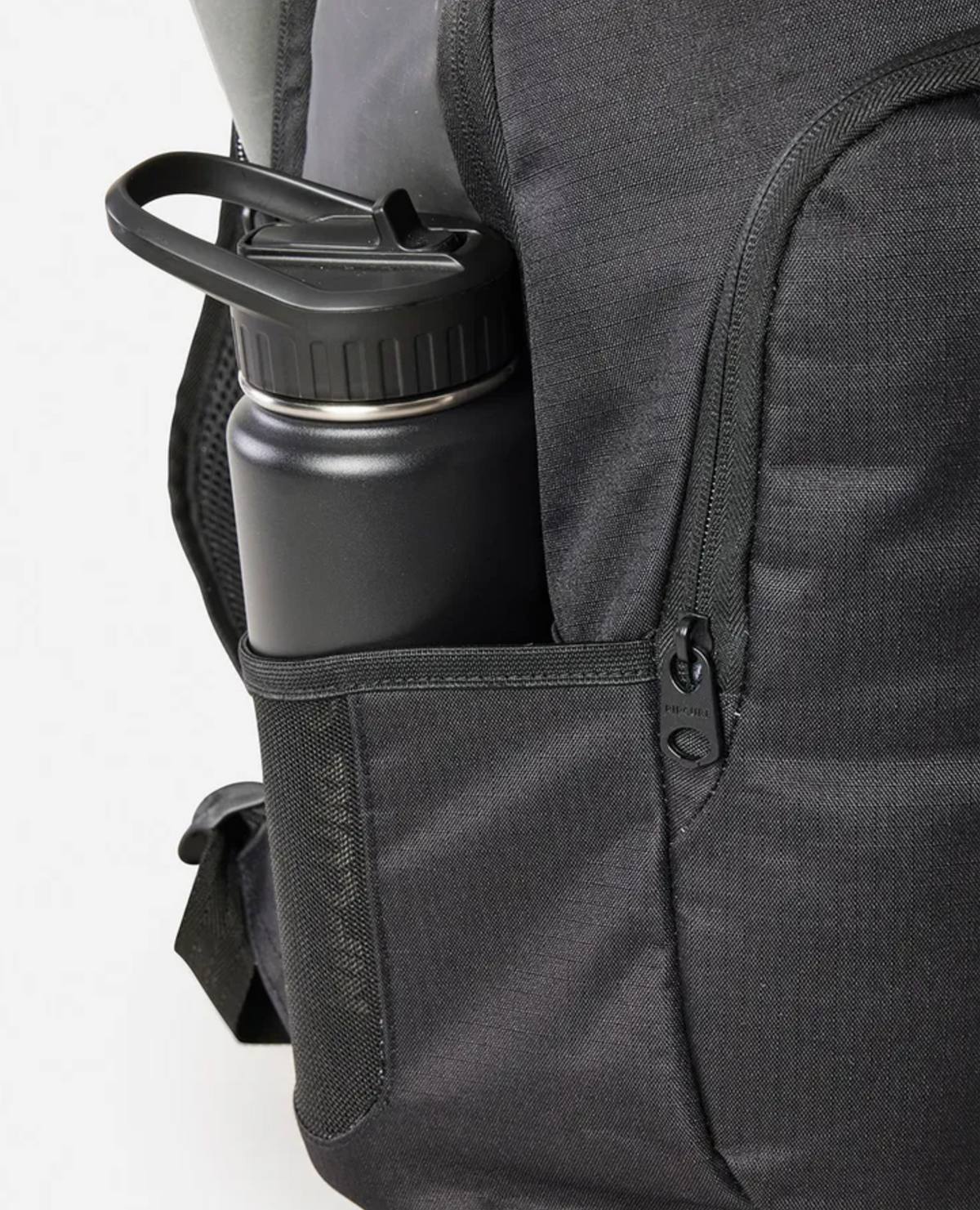 A Rip Curl Ozone Icons 30L Backpack in black features a side pocket holding a matte black water bottle with a handle. The partially open zipper reveals subtly textured fabric and organized compartments for essentials.