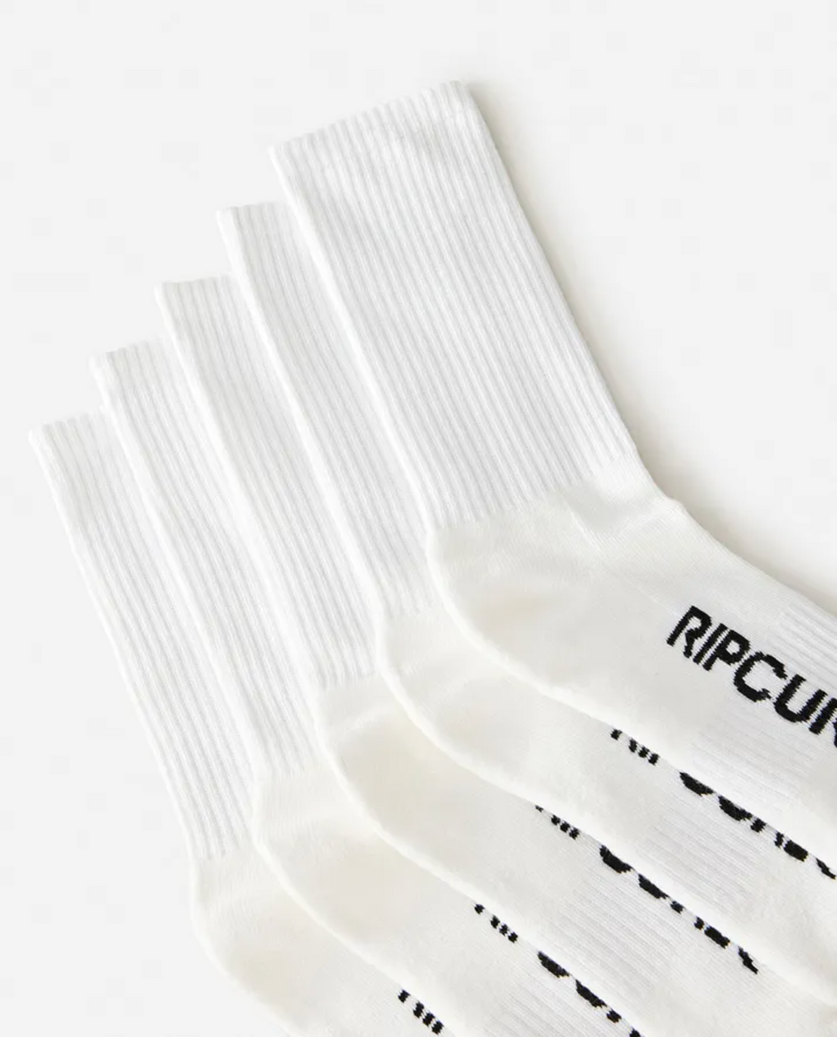 Five pairs of white Rip Curl School Crew Socks are stacked diagonally, toes pointing right. The black "RIP CURL" logo appears on the top sock near the toes, showcasing their terry footbed and built-in arch support.