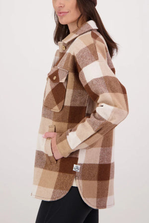 A woman stands sideways with one hand in her pocket, modeling the Swanndri Anchorage V3 Womens Wool Shacket in brown, beige, and white premium New Zealand wool against a plain background.