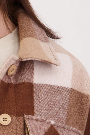 Close-up of a person with long brown hair wearing the Swanndri Anchorage V3 Womens Wool Shacket in brown and beige plaid, made from premium New Zealand wool. It features large buttons, a pointed collar, and a visible pocket flap.
