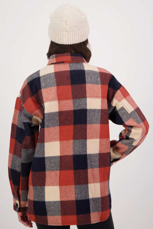 A person in a cream knit beanie is wearing a red, cream, and navy plaid Swanndri Anchorage v2 Wool Shirt Jacket. They are facing away against a plain light background.