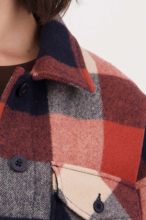 Close-up of someone wearing a Swanndri Anchorage v2 Wool Shirt Jacket with large red, navy, and beige checks. The wool complements the black buttons and front pocket. The person's neck is visible, enhancing the cozy merino blend look.