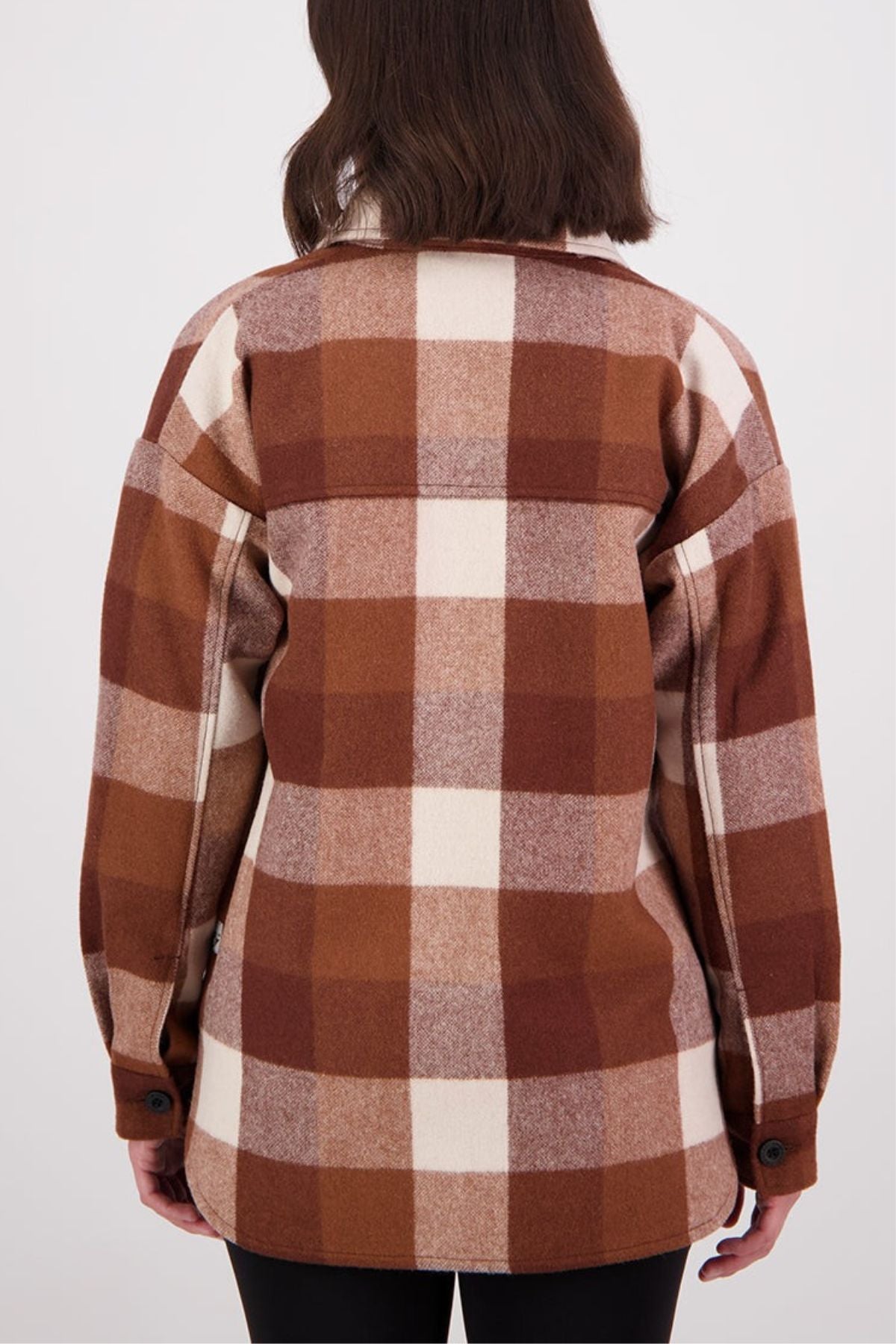 A person with shoulder-length brown hair is shown from the back, wearing a Swanndri Anchorage v2 Wool Shirt Jacket in brown, beige, and cream plaid with black buttons, standing against a plain light background.
