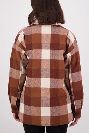 A person with shoulder-length brown hair is shown from the back, wearing a Swanndri Anchorage v2 Wool Shirt Jacket in brown, beige, and cream plaid with black buttons, standing against a plain light background.