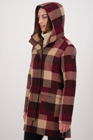 Dressed in a Swanndri Annmore V2 Wool Overcoat with a large burgundy, brown, and beige check pattern over a white turtleneck, a person stands against a plain light background.