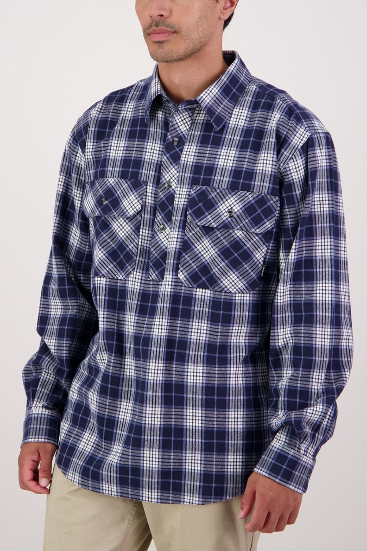 A man wearing the Swanndri Barn Shirt, a blue and white plaid 100% cotton shirt with two chest pockets ideal for winter layering, stands against a plain light background.